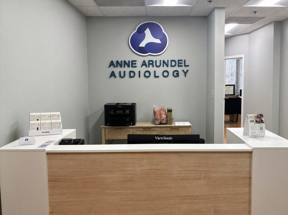 Reception desk beneath the Anne Arundel Audiology wall sign at the Glen Burnie, MD hearing clinic